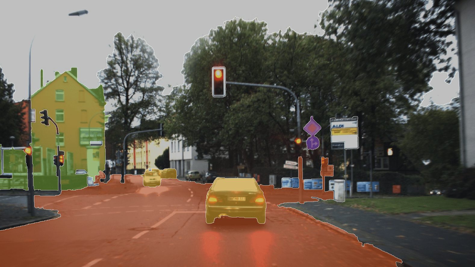 A car waits at a red light on a tree-lined urban street with buildings and traffic signs highlighted in various colors, an ideal scene for testing SemanticKITTI's capabilities.