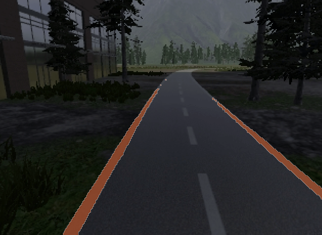 A road, undergoing pavement maintenance to address road damage, is surrounded by trees and a building on the left side. It leads into a forested area with mountains in the background.