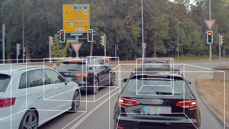 Several cars waiting at a signalized intersection with a yellow road sign in the background, surrounded by trees, reminiscent of scenes used in A2D2 datasets.