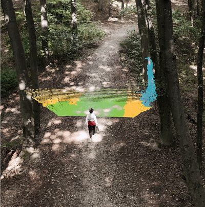 A person walking on a forest trail, with an overlay of colored point cloud data visualizing sensor data in front of them.