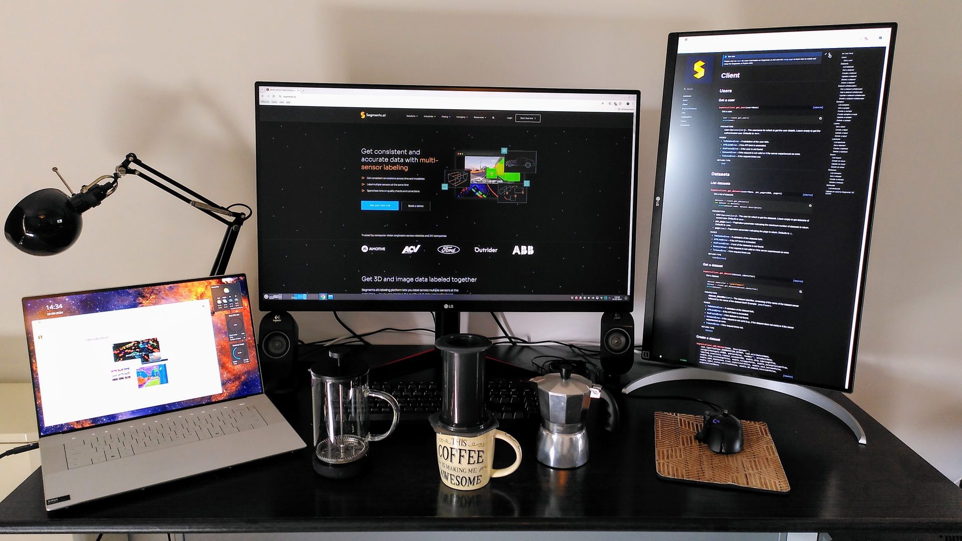 Remote desk machine learning engineer A workspace with dual monitors, a laptop, coffee equipment, and a desk lamp, set up for productivity.