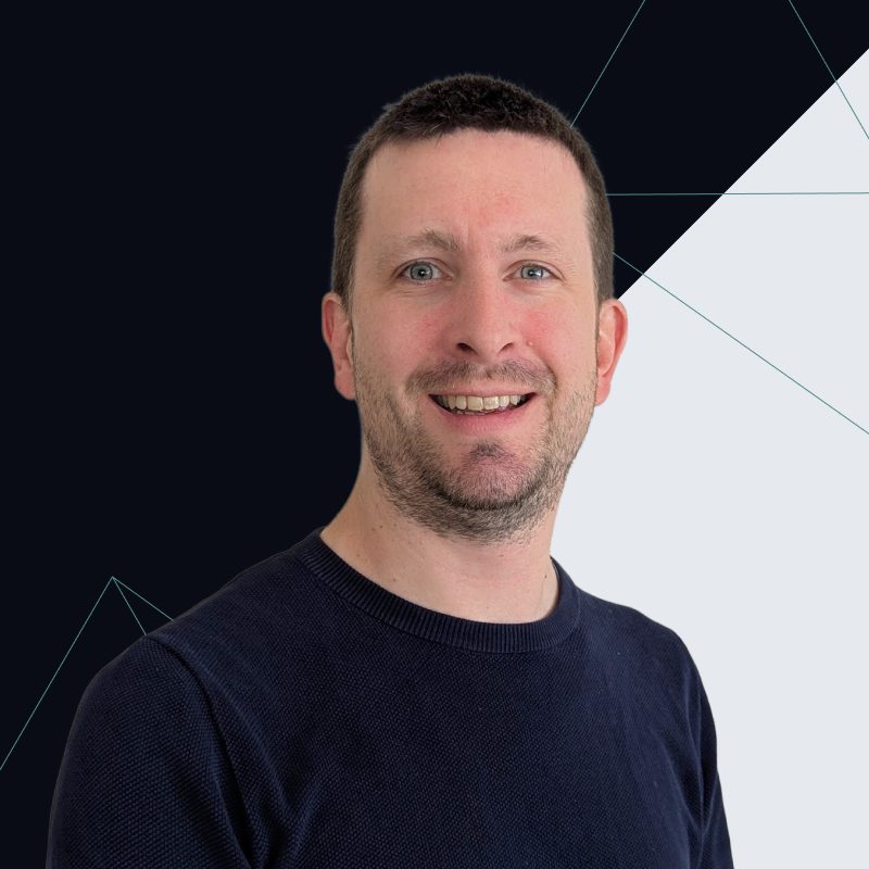 Smiling man with short brown hair and beard, wearing a dark sweater, on a geometric background.